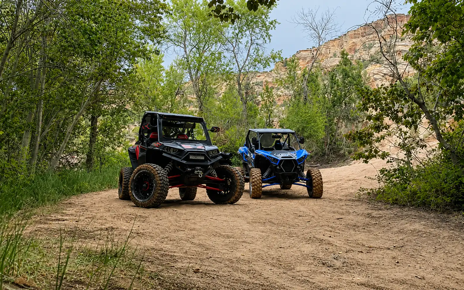 Two side-by-side UTVs on the sandy Doc's Beach trail below red-rock cliffs near Vernal, Utah